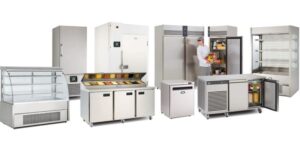 A row of commercial refrigeration equipment, including display cases, prep counters, upright refrigerators, and freezers. A person in chef attire is placing items inside one of the refrigerators.