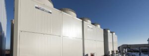 Large white Mitsubishi CITY MULTI HVAC units installed on a rooftop under a clear blue sky, with pipes and additional equipment visible beside them.