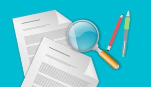 Two sheets of paper, a magnifying glass, a red pencil, and two pens are arranged on a blue background, suggesting examination or review of documents.